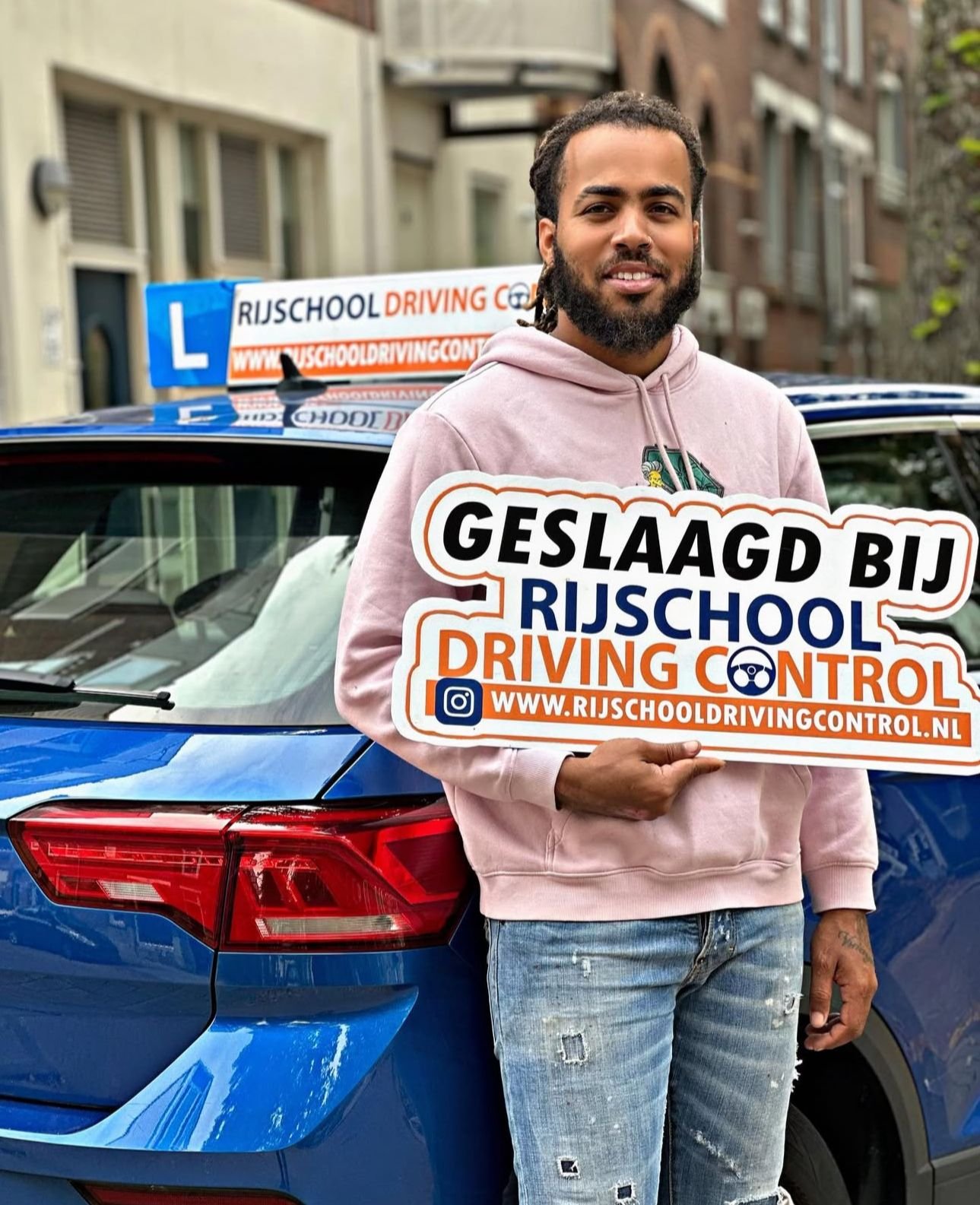 Geslaagde leerling met Geslaagd-bord naast blauwe lesauto van Rijschool Driving Control in Rotterdam — autorijbewijs B behaald