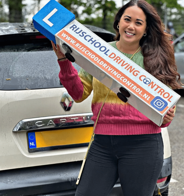 Vrouwelijke geslaagde leerling met Rijschool Driving Control reclamebord bij lesauto Rotterdam — rijbewijs B schakel behaald